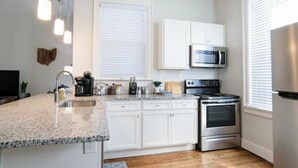 A modern kitchen with white cabinets, a stainless steel stove, a microwave, and a granite countertop.