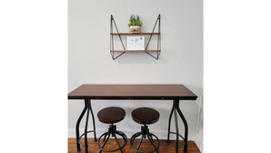 A table with two stools, a shelf with a plant, and a sign with text.
