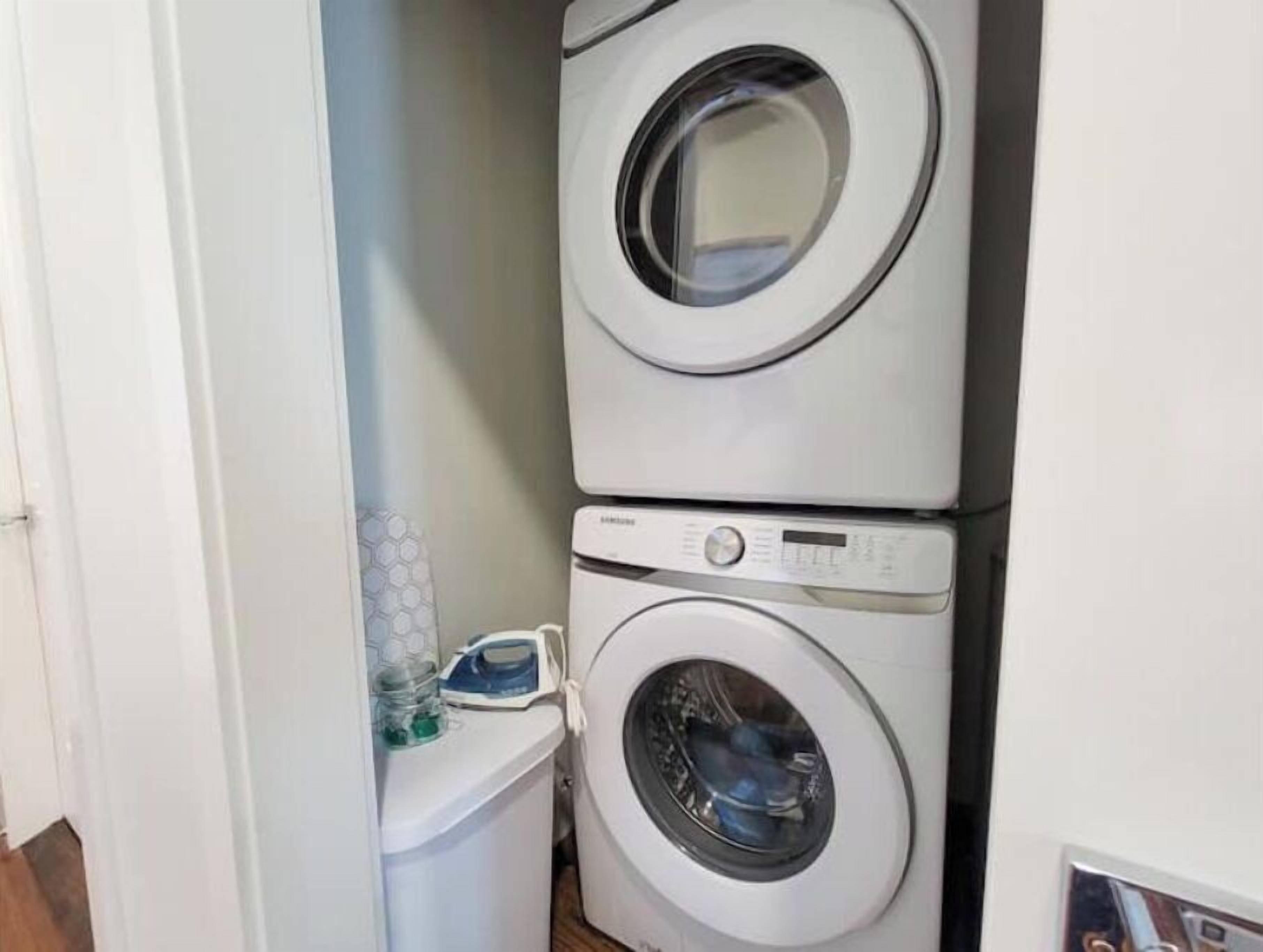 A laundry room with two stacked washing machines and a small shelf with cleaning supplies.