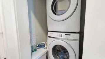 A laundry room with two stacked washing machines and a small shelf with cleaning supplies.