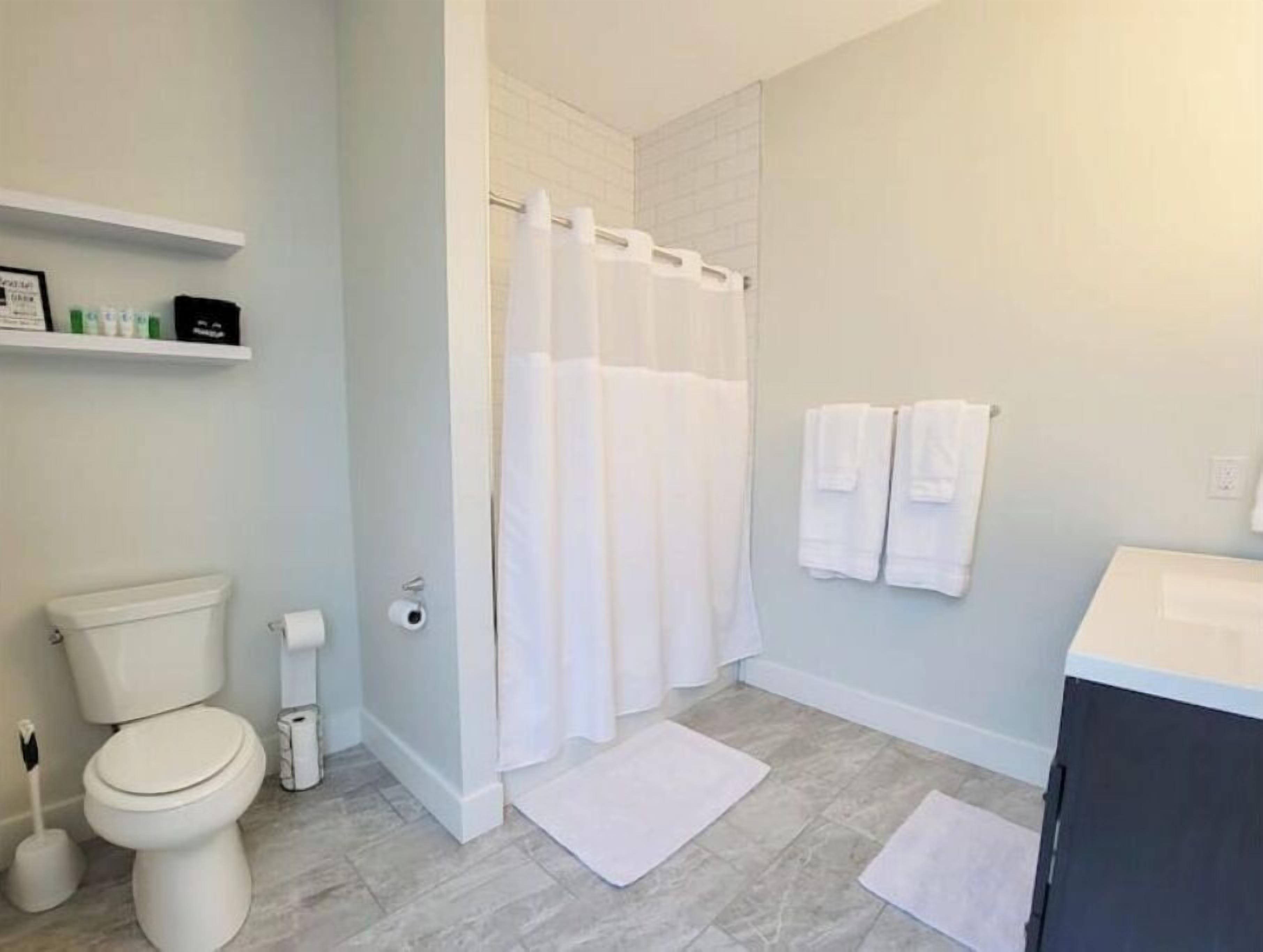 A bathroom with a toilet, a shower with a white curtain, a sink, and two white towels on the wall.