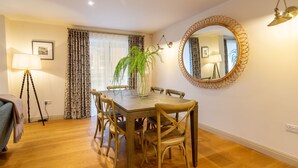 Un comedor con una mesa y sillas de madera, un florero con una planta, un espejo redondo en la pared y una lámpara.
