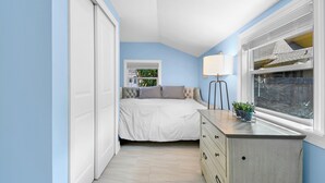 Un dormitorio con cama, cómoda, ventana y lámpara.