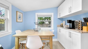 Una cocina con pared azul claro, gabinetes blancos, una mesa de madera y sillas blancas.