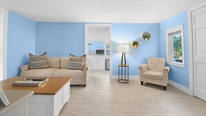 Un salón con un sofá color beige, una mesa de centro de madera, un sillón color beige y una mesita auxiliar con una lámpara.