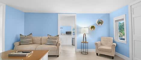 Een woonkamer met een beige bank, een houten salontafel, een beige fauteuil en een bijzettafeltje met een lamp.