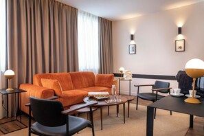 A modern hotel room with a sofa, chairs, a coffee table, a desk, and a lamp. - Hotel du Port (Nogent-sur-Marne)