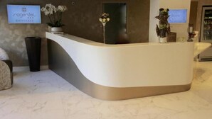 A reception desk with a curved design, a sign reading "Nogentel," and a potted plant with white flowers. - Hotel du Port (Nogent-sur-Marne)