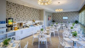 A modern dining area with white chairs and tables, a buffet station, and decorative wall patterns. - Hotel du Port (Nogent-sur-Marne)