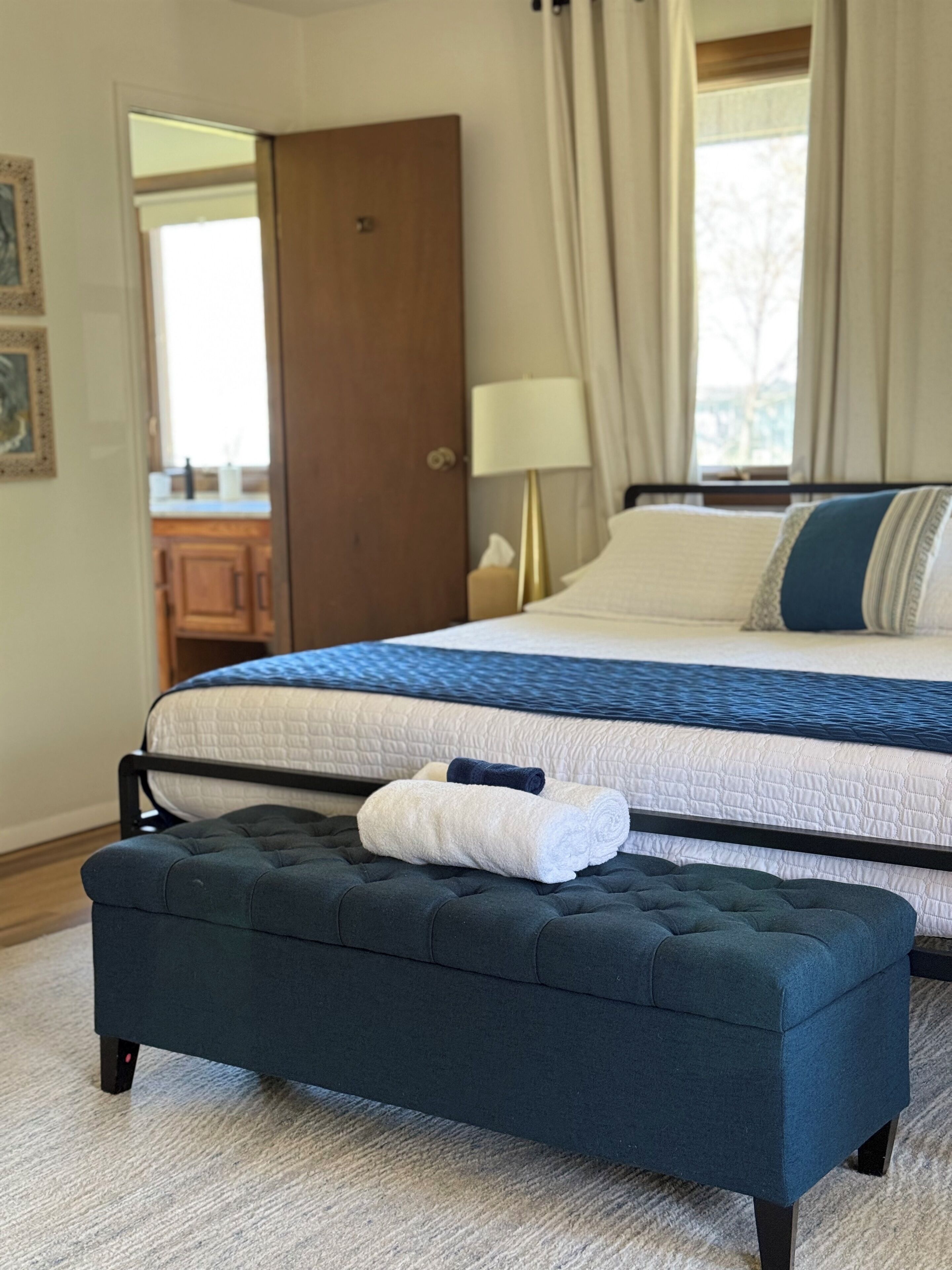 A bedroom with a bed, a bench, a lamp, and a door.
