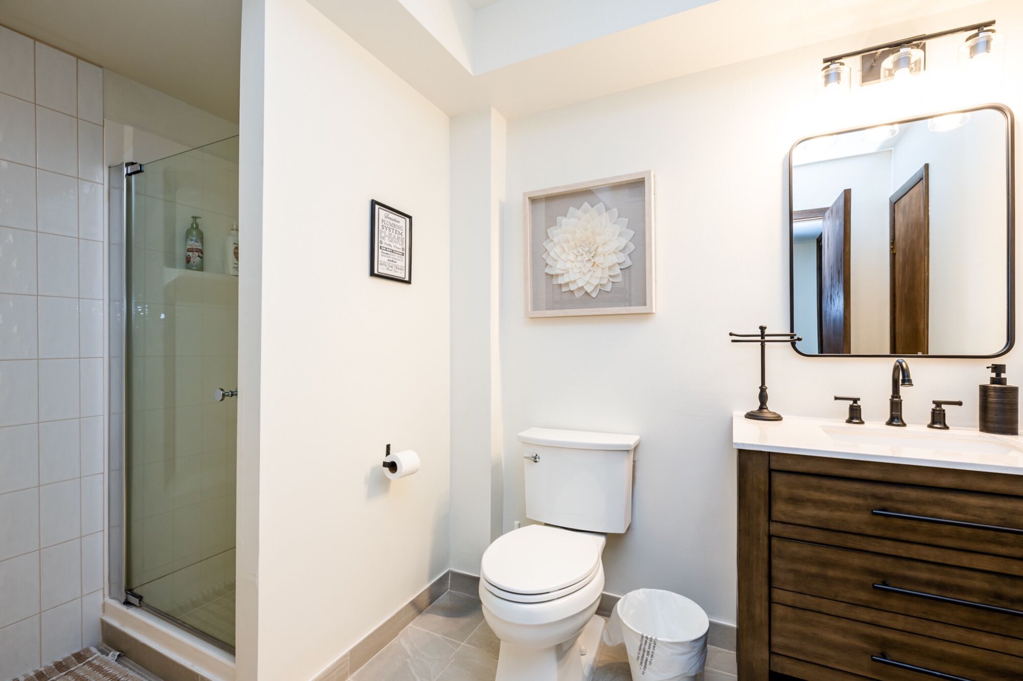 Ein modernes Badezimmer mit einer Duschkabine aus Glas, einer Toilette, einem Waschbecken mit Spiegel und einem gerahmten Kunstwerk an der Wand.