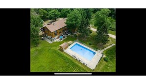 An aerial view of a two-story house with a swimming pool, surrounded by greenery and a paved driveway. - Spacious 4BR Retreat • Private Beach • Heated Outdoor Pool is OPEN • Golf Cart (Coloma)
