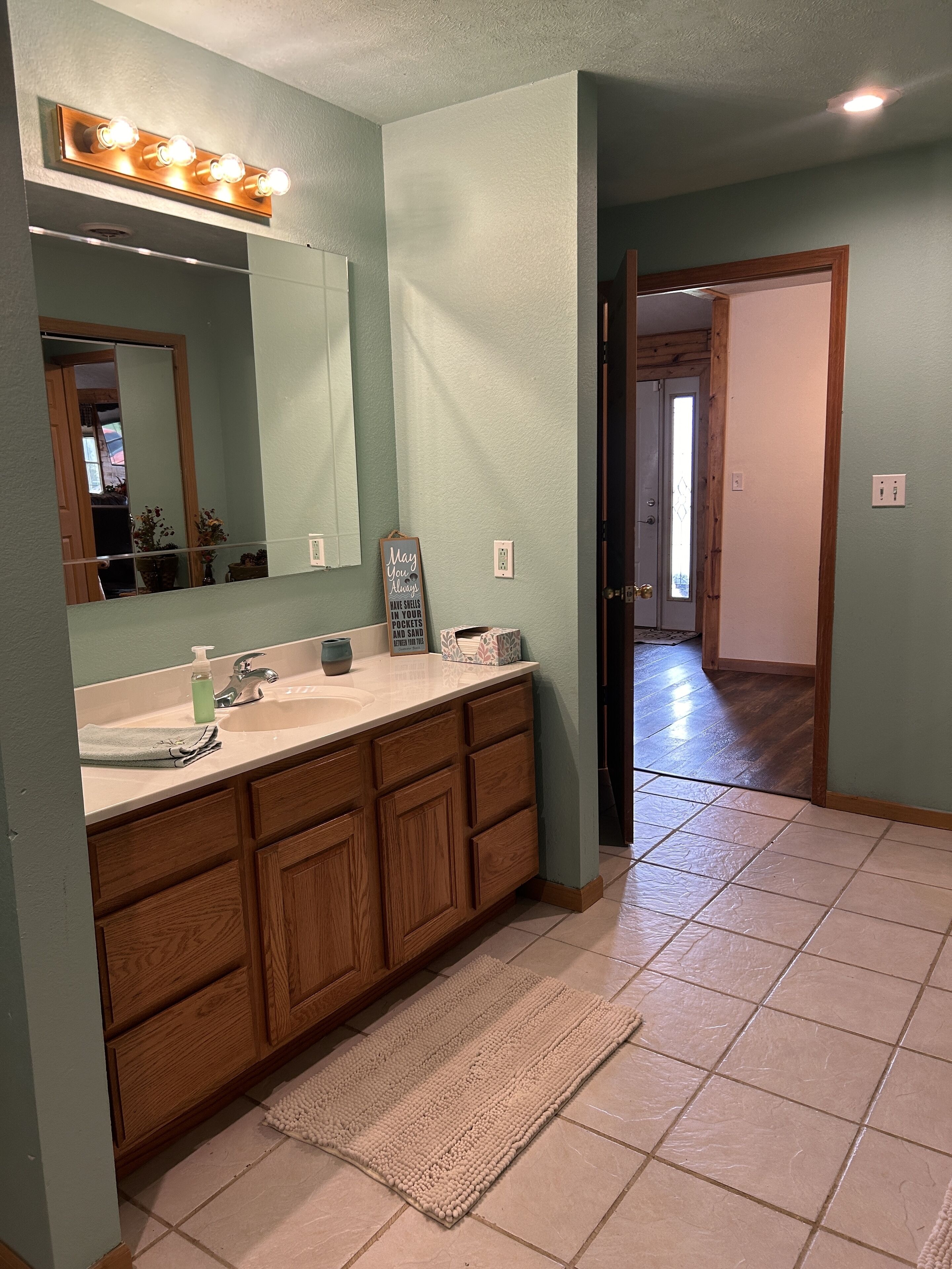 A bathroom with a double vanity, a large mirror, and a lighted vanity area.