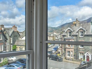 A view through a window of a street with parked cars, stone buildings, and a mountain in the background. - Enjoy a family holiday right here in the heart of the Lake District. (Keswick)