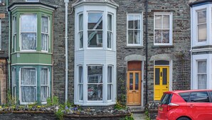A row of stone houses with bay windows, a red car parked in front, and a yellow door. - Enjoy a family holiday right here in the heart of the Lake District. (Keswick)