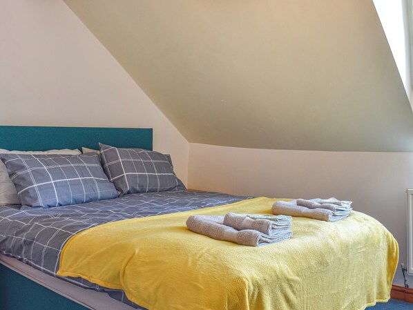 A neatly made bed with a blue and gray checkered bedspread, a teal headboard, and a yellow blanket.