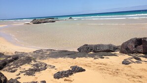 A beach with clear skies, calm waters, and large rocks in the foreground. - Holiday flat in a beautiful complex with large swimming pool and private terrace (Corralejo)