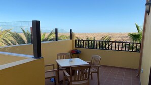 A balcony with a table and chairs, a TV, and a view of the beach. - Holiday flat in a beautiful complex with large swimming pool and private terrace (Corralejo)