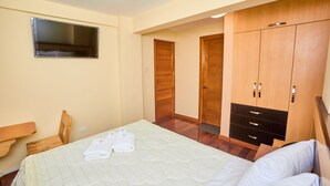 A bedroom with a bed, wooden wardrobe, and a television on the wall.