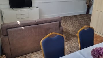 Ett vardagsrum med en soffa, två fåtöljer, en tv som står på ett skåp och en mönstrad matta.