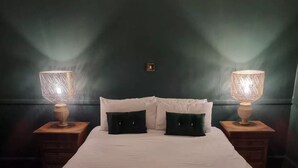 Ein ordentlich bezogenes Bett mit weißer Bettwäsche und zwei schwarzen Kissen, an beiden Seiten zwei Nachttische mit Lampen.
