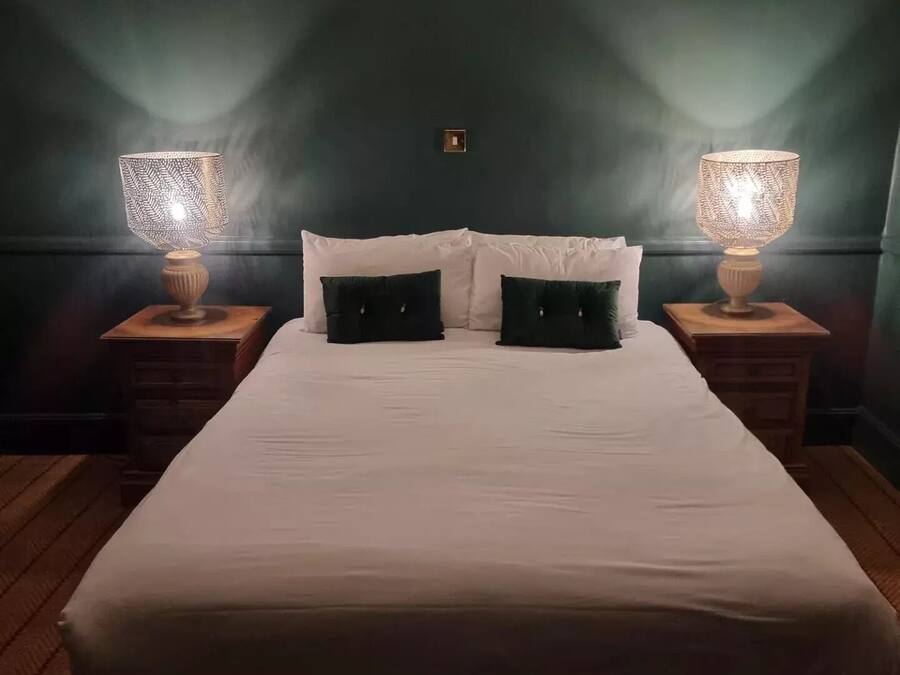 A neatly made bed with white bedding and two black pillows, flanked by two bedside tables with lamps.