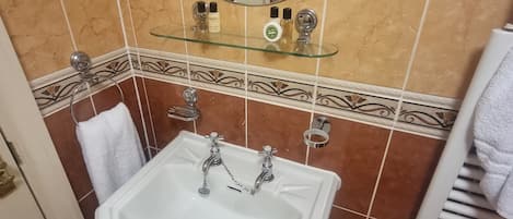 A bathroom with a white sink, a mirror, and a glass shelf with toiletries.