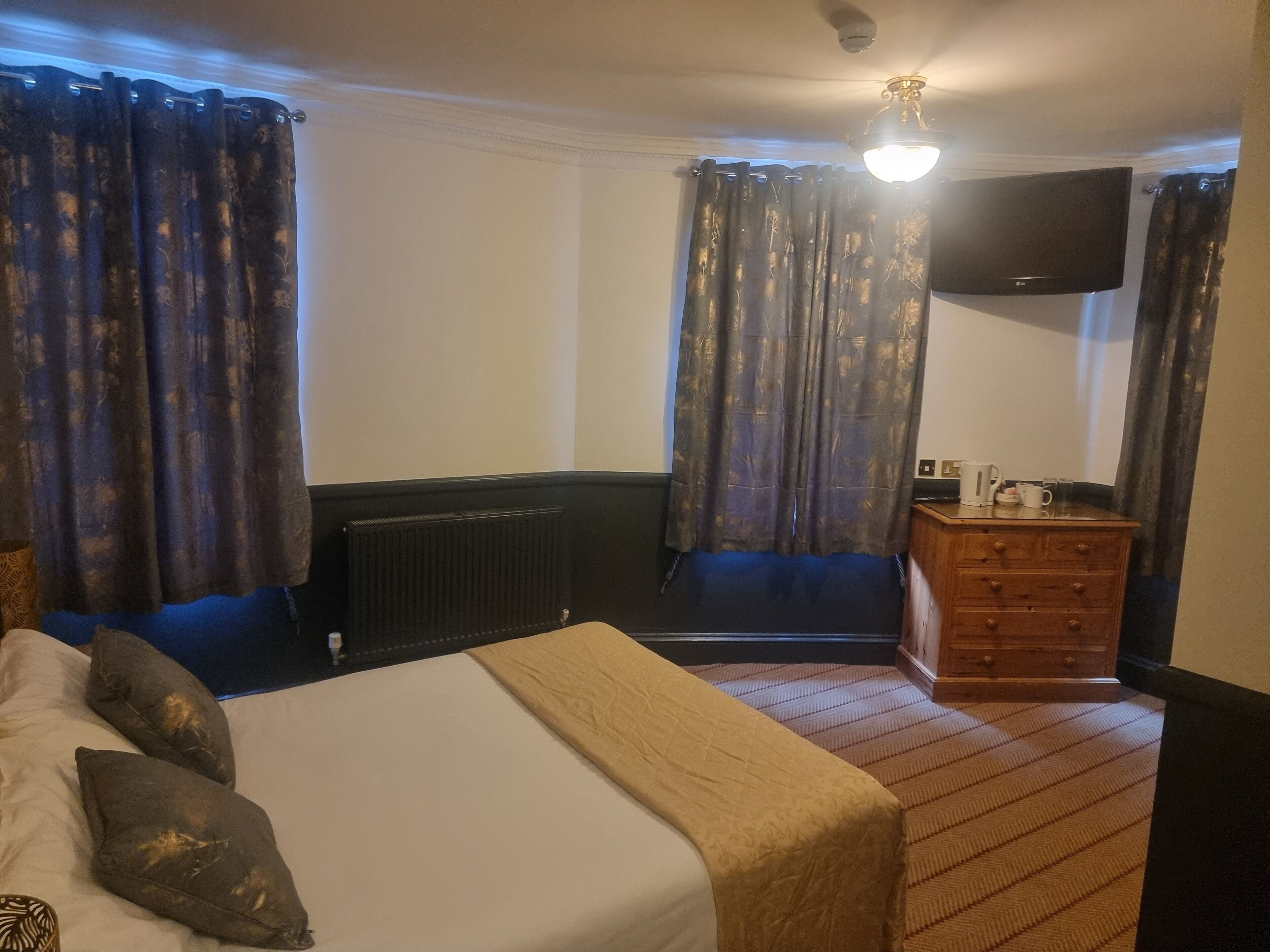 A hotel room with a bed, a dresser, a radiator, a television, and curtains.