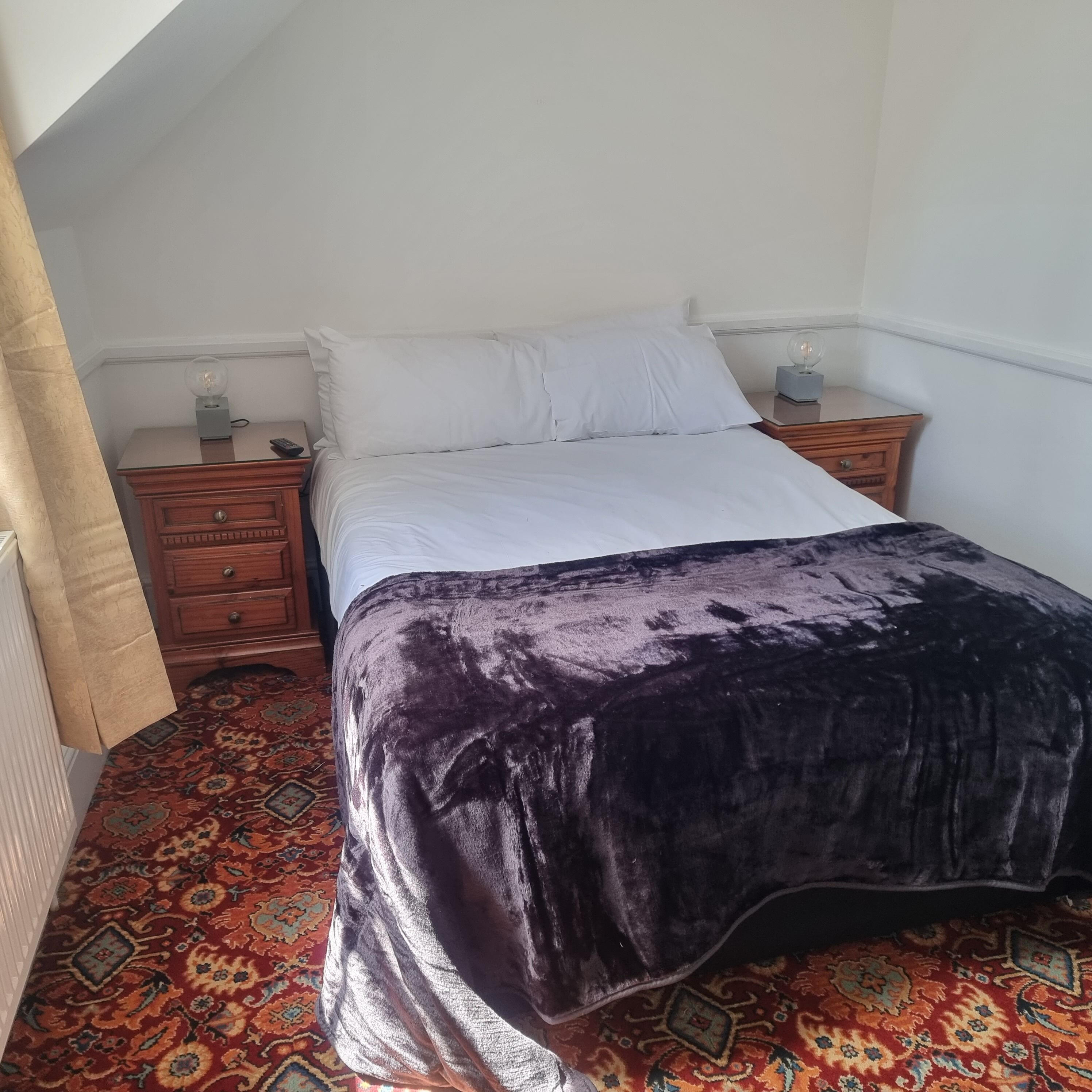 Een slaapkamer met een bed, nachtkastjes, een lamp en een kamerkleed met een patroon.