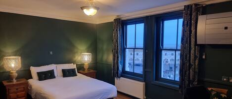 Habitación de hotel con una cama grande, dos lámparas de noche, una ventana con cortinas y vistas a edificios.