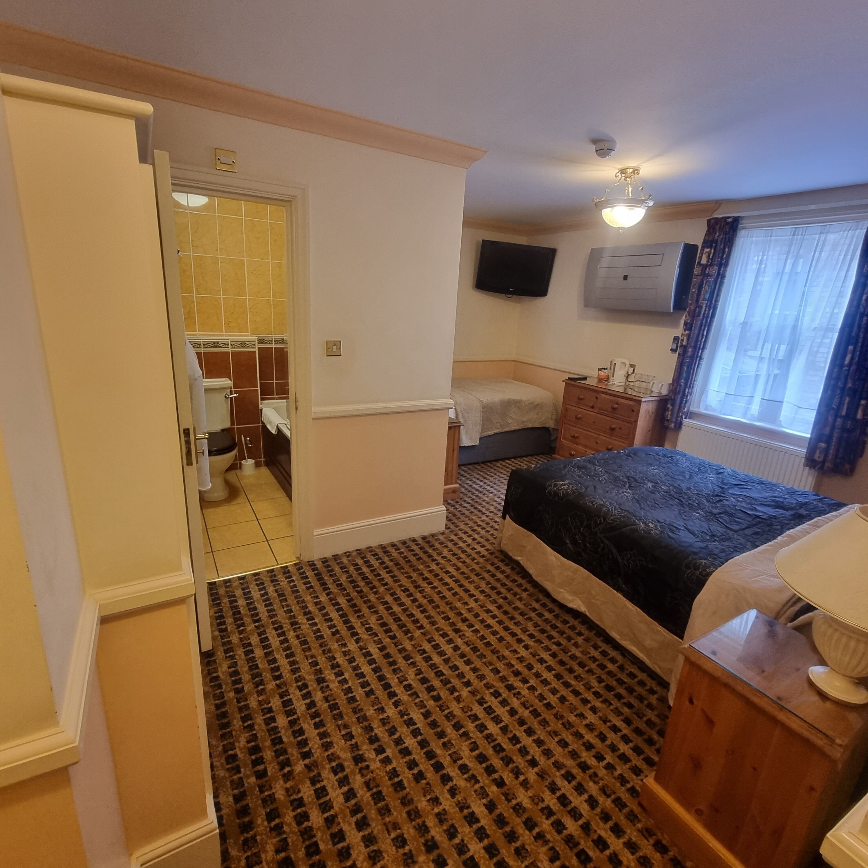 Una habitación de hotel con una cama, un tocador, un televisor y una ventana con cortinas.