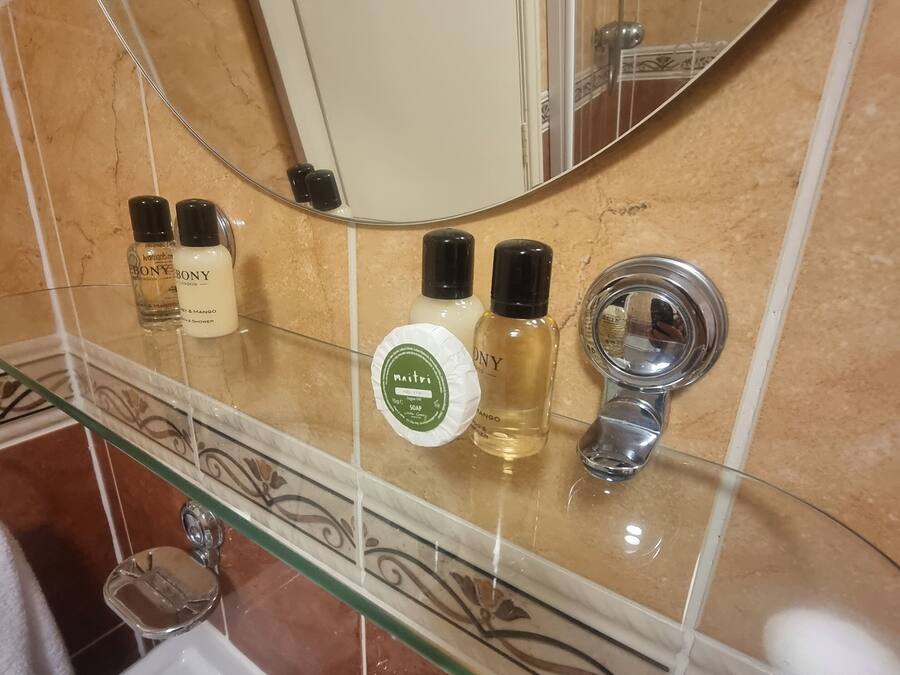 Kylpyhuoneessa on lasihylly, jossa on hygieniatuotteita, peili ja pesuallas hanalla.