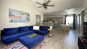 A modern living room with a blue sectional sofa, a ceiling fan, and a kitchen in the background.