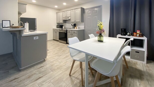 A modern kitchen with grey cabinets, a white dining table, and a vase of flowers.