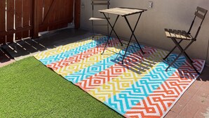 A patio area with a colorful patterned rug, a small folding table, two folding chairs, and a green artificial turf.