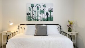 A neatly made bed with white bedding, two bedside tables with lamps, a wall-mounted artwork, and a vase with flowers on a nightstand.