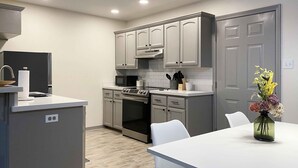 A modern kitchen with grey cabinets, a white countertop, a built-in oven, and a dining area with a white table and chairs.