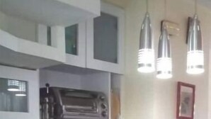 A kitchen with white cabinets, a black countertop, a built-in oven, a sink, and hanging pendant lights.