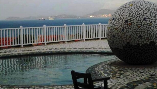 A pool area with a mosaic ball sculpture, a white fence, and a view of the sea.