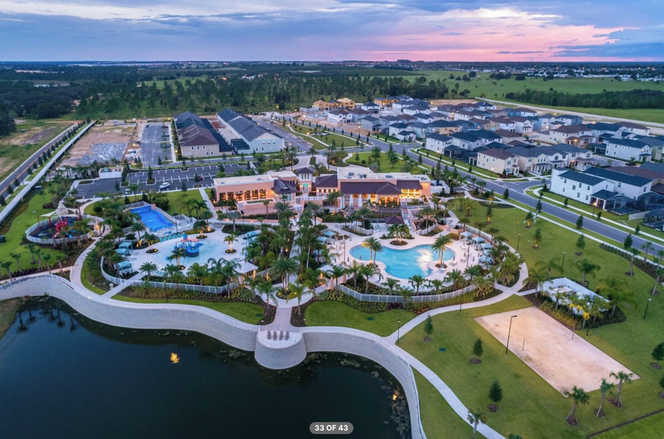 Vue aérienne d’un quartier résidentiel avec une grande piscine, plusieurs maisons et un parc bien entretenu.