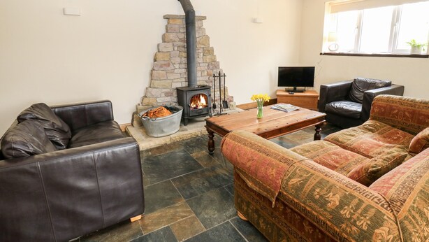 A cozy living room with a stone fireplace, leather sofas, and a television. - The Bike Shed (High Peak)
