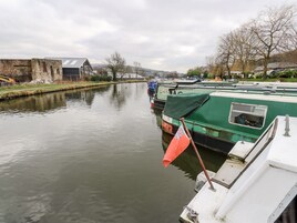 Un canal tranquilo con barcos amarrados a la orilla, un pequeño edificio con techo inclinado y un cielo despejado.