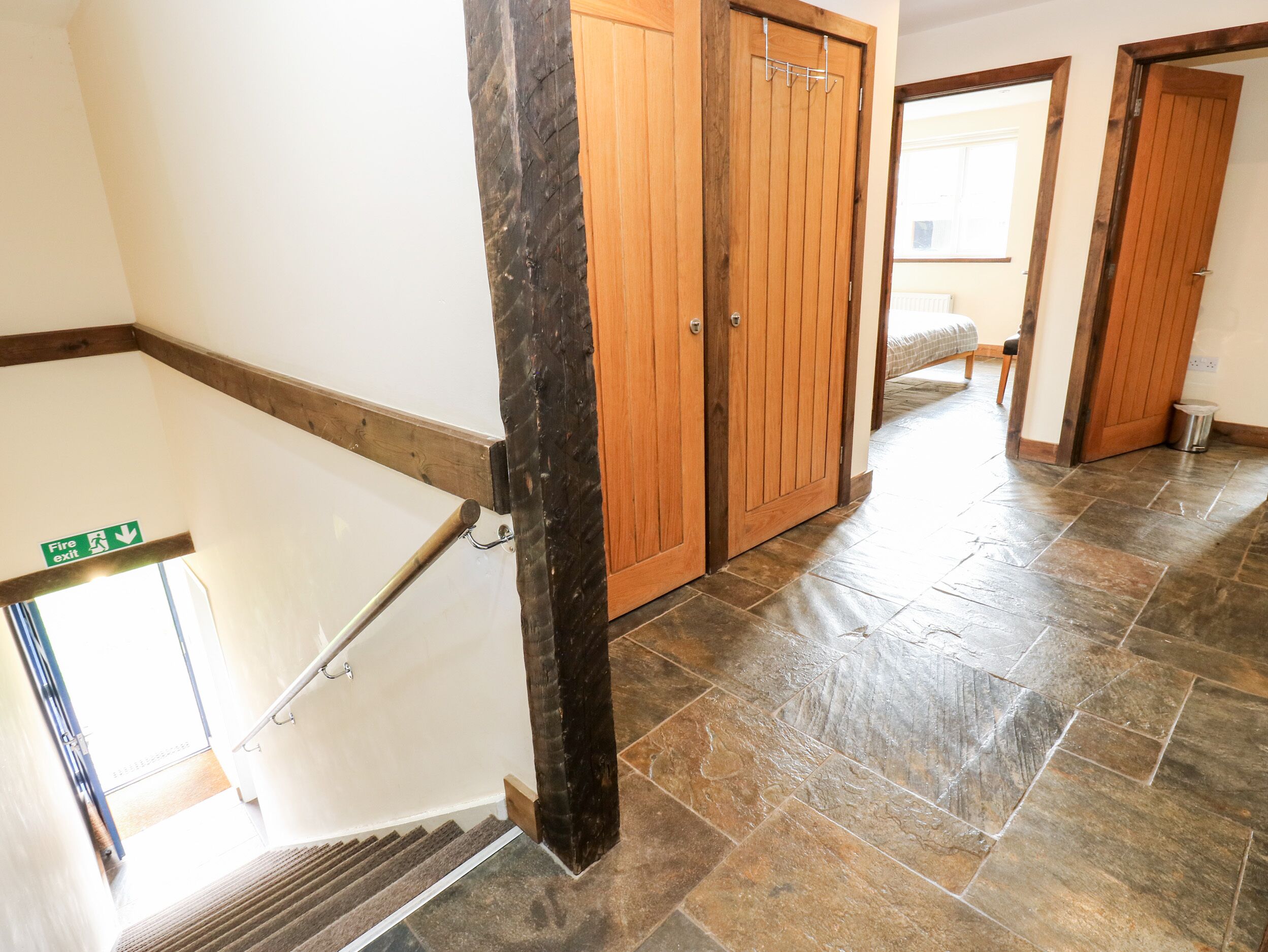 Un couloir avec un panneau indiquant la sortie de secours, des portes en bois et un sol carrelé.