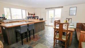 A modern kitchen with a bar area, a dining table with chairs, and a view of the outdoors. - The Bike Shed (High Peak)