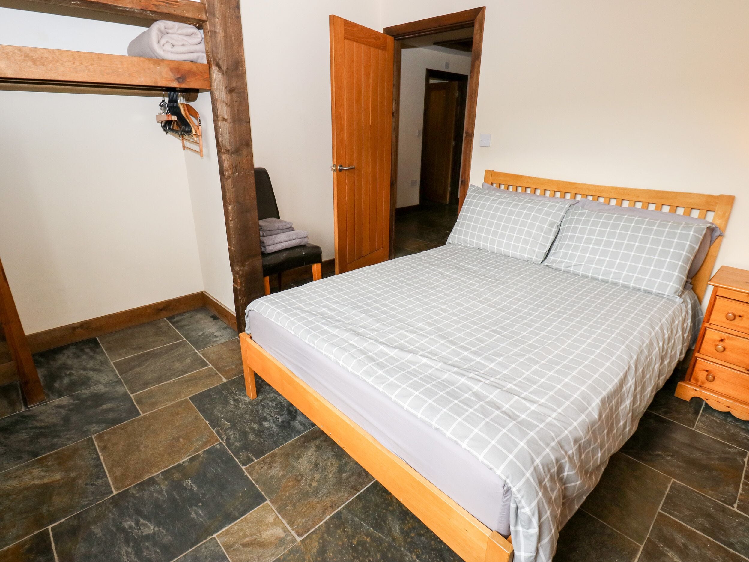 Un dormitorio con una cama de madera, un banco, una puerta y una estantería en la pared.