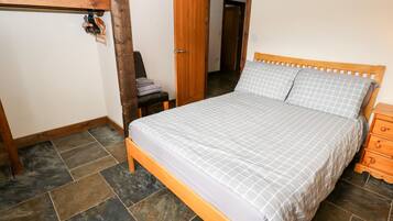 Un dormitorio con una cama de madera, un banco, una puerta y una estantería en la pared.