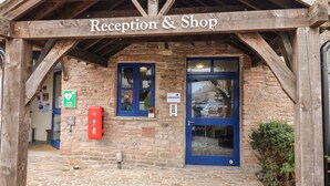 A reception and shop area with a stone wall, wooden beams, a blue door, and emergency contact signs. - The Bike Shed (High Peak)