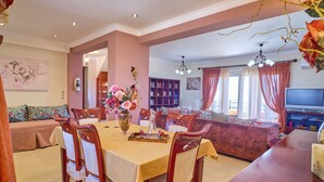 Un coin repas avec une table dressée pour quatre personnes, entouré de chaises en bois, d’une bibliothèque et d’un téléviseur en arrière-plan.