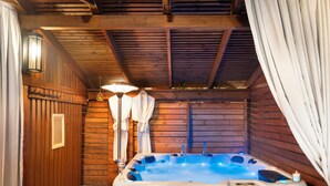 Une cabane en bois dotée d’un bain à remous, de murs en bois et d’un plafond avec des poutres apparentes.