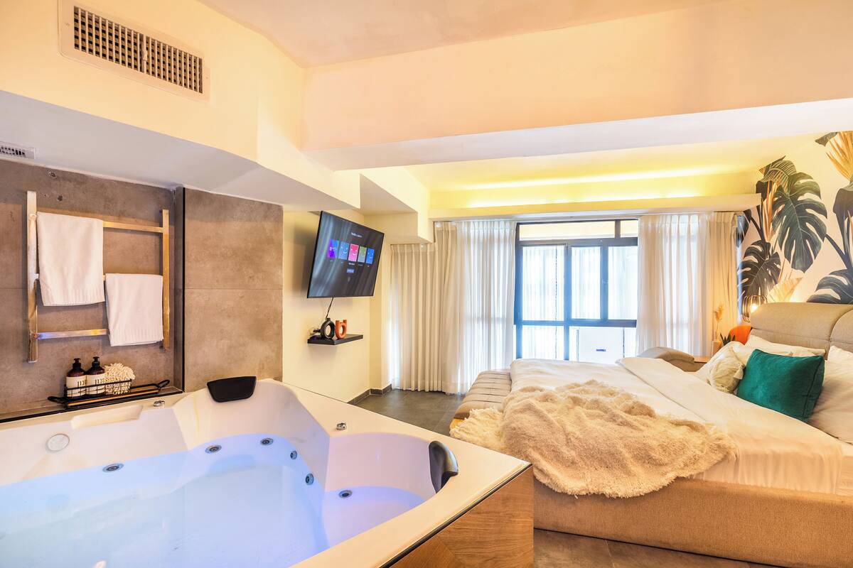 Une chambre d’hôtel moderne dotée d’une grande baignoire, d’un canapé avec une couverture moelleuse, d’un téléviseur à écran plat et d’une grande fenêtre avec des rideaux.